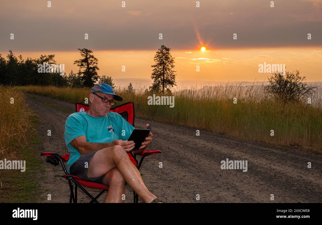 Un maschio adulto si rilassa mentre legge su un libro Kindle a Spring Mountain nella catena montuosa Blue Mountain dell'Oregon centrale. Foto Stock