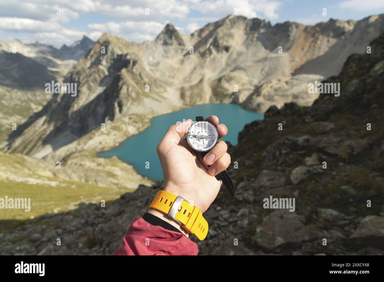 La mano di un uomo regge una bussola magnetica tascabile per navigare sullo sfondo di un pendio roccioso e di un lago di montagna. Il concetto di trovare un modo. G Foto Stock