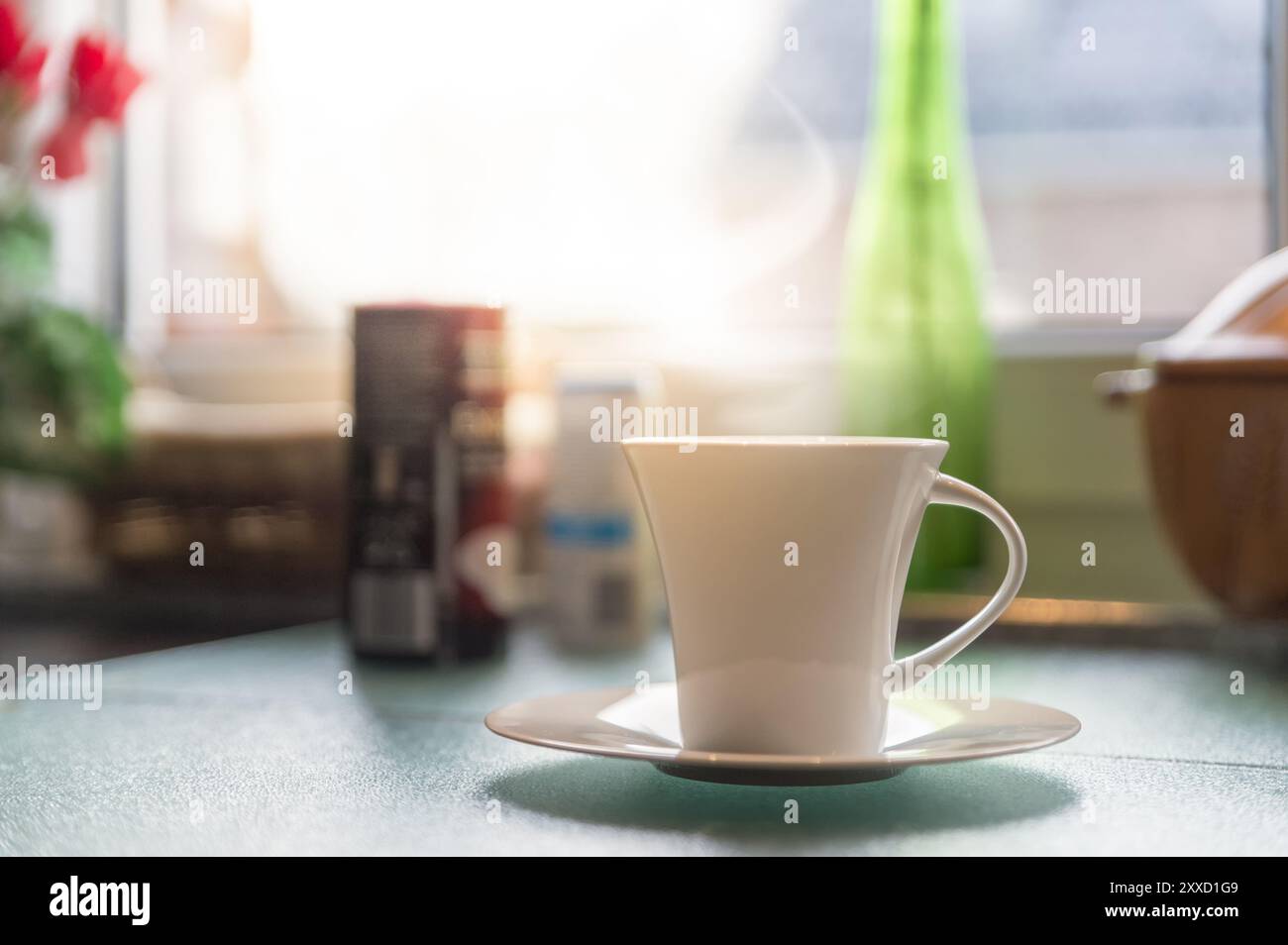 Una tazza di caffè e un contenitore per cialde di caffè si appoggiano alla luce di fronte alla finestra della cucina Foto Stock