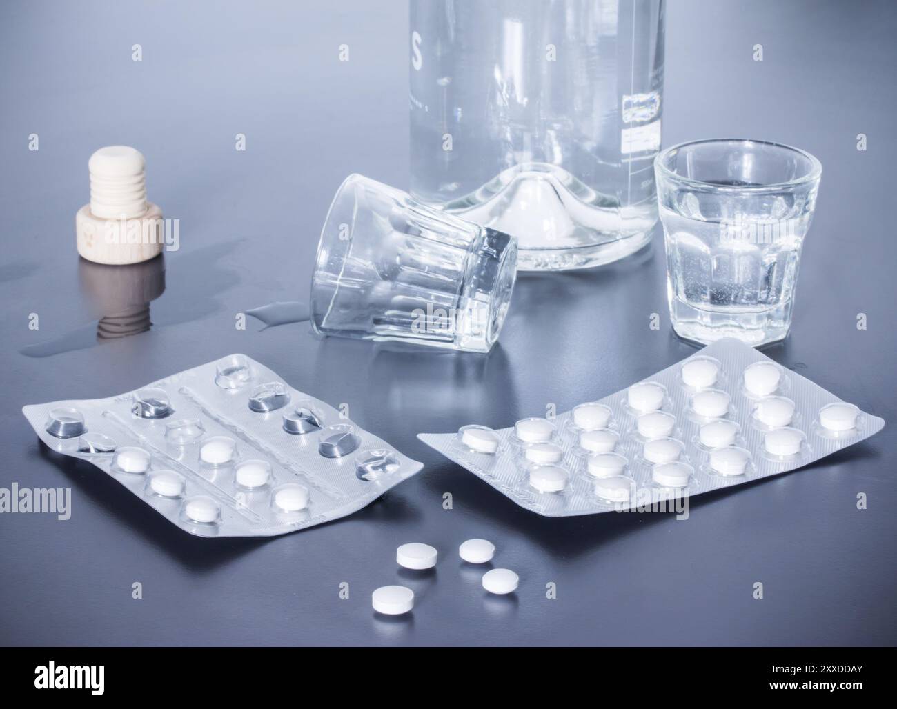 Pillole e alcol su un tavolo grigio. Concetto di abuso di droga Foto Stock