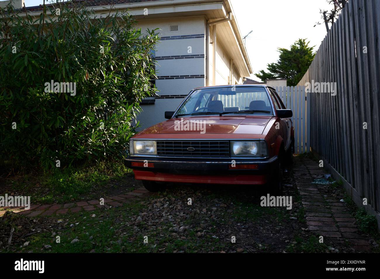 Vecchia berlina rossa Ford Meteor, senza targhe, parcheggiata in un vialetto fuori da una casa suburbana, circondata dalla vegetazione Foto Stock