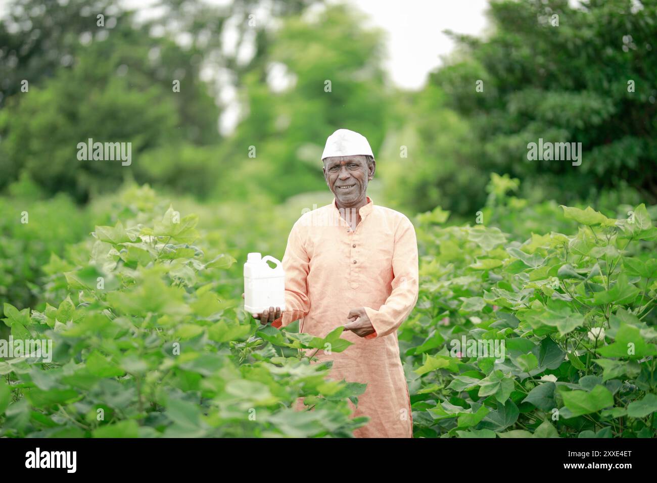 Felice contadino villaggio indiano che detiene la bottiglia di fertilizzante guardando la fotocamera a terreno agricolo - concetto di promozione del prodotto, raccomandazione e agricolo Foto Stock