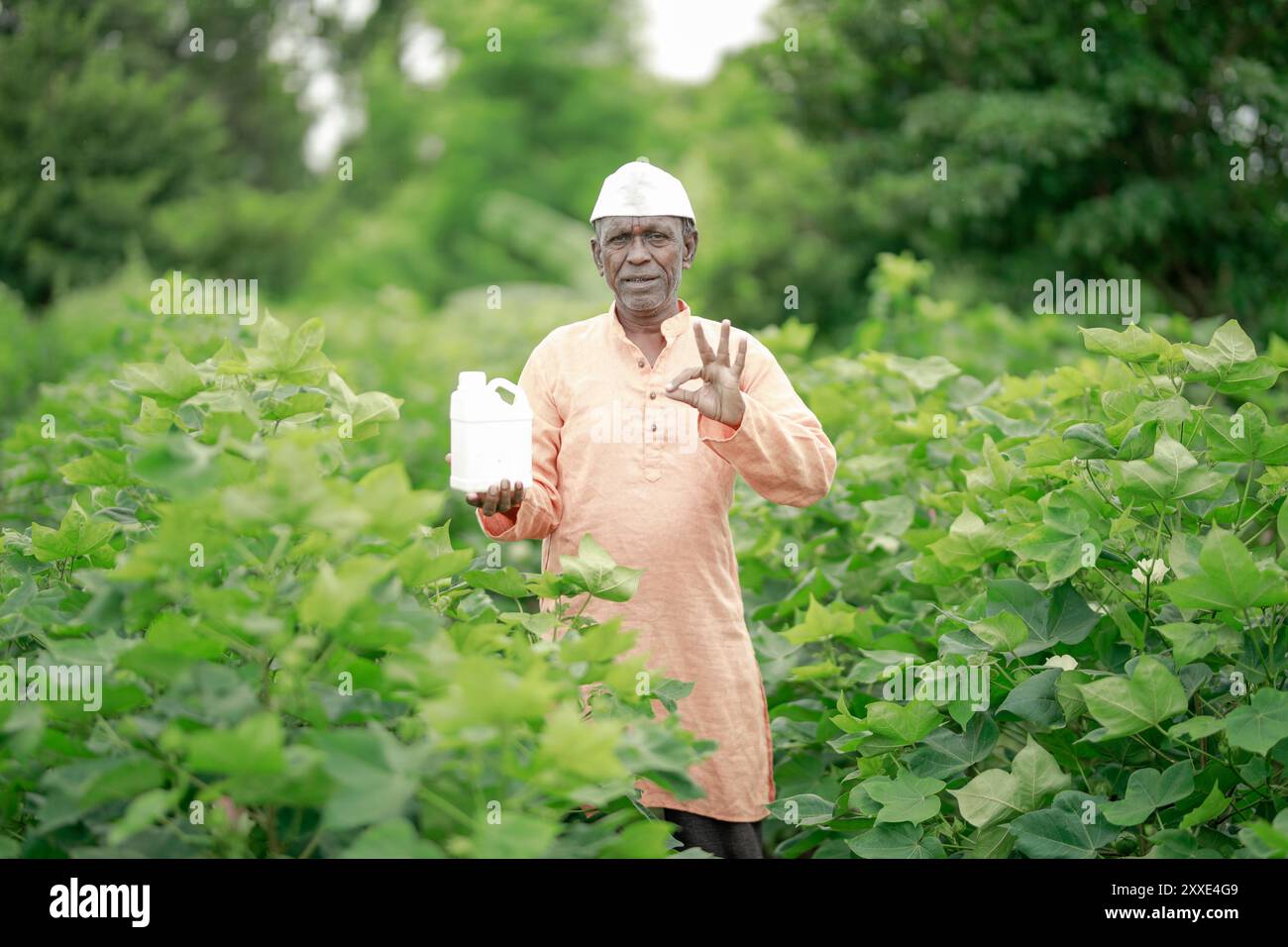 Felice contadino villaggio indiano che detiene la bottiglia di fertilizzante guardando la fotocamera a terreno agricolo - concetto di promozione del prodotto, raccomandazione e agricolo Foto Stock