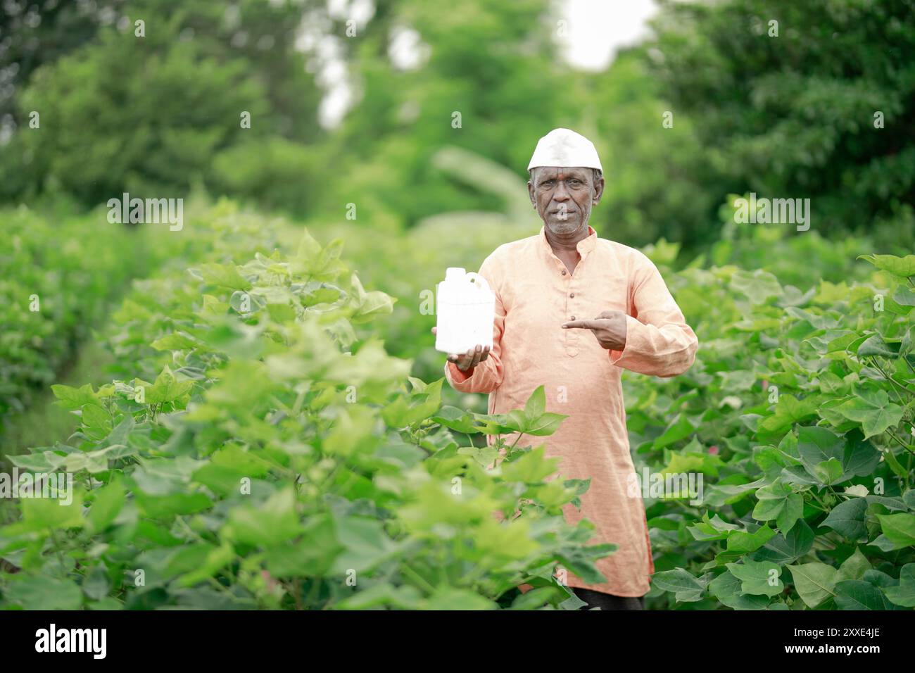 Felice contadino villaggio indiano che detiene la bottiglia di fertilizzante guardando la fotocamera a terreno agricolo - concetto di promozione del prodotto, raccomandazione e agricolo Foto Stock