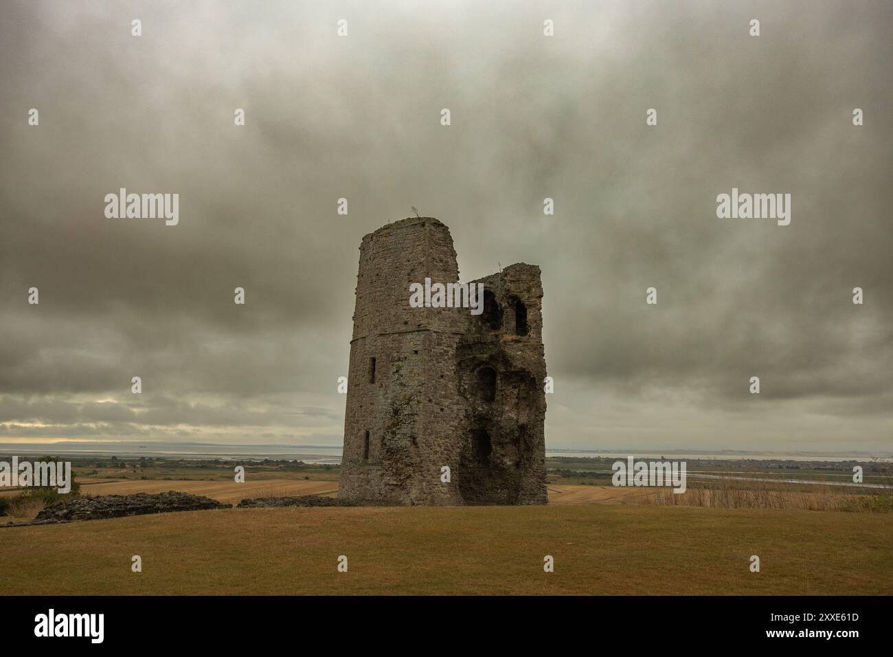Castello di Hadleigh, Regno Unito. 24 agosto 2024. Una torre di pietra solitaria e resistente agli agenti atmosferici sorge in un campo piatto e aperto sotto un cielo nuvoloso e coperto. La struttura, forse un residuo di una fortificazione medievale o di un castello, mostra segni di erosione e crollo. Il paesaggio circostante è ampio e desolato, evocando temi di isolamento storico e degrado rurale. Un inizio bagnato e cupo per il fine settimana festivo al Castello di Hadleigh, affacciato sull'estuario del Tamigi. Penelope Barritt/Alamy Live News Foto Stock