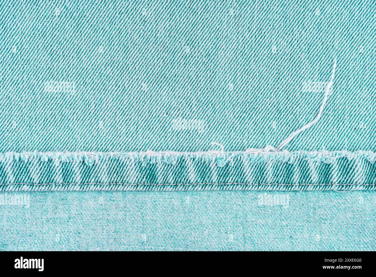 Pantaloni in denim turchese con bordo shabby su fondo in tessuto jean, primo piano, effetto macro. Jeans strappati, distrutti strappati. Sfondo, sfondo, design de Foto Stock