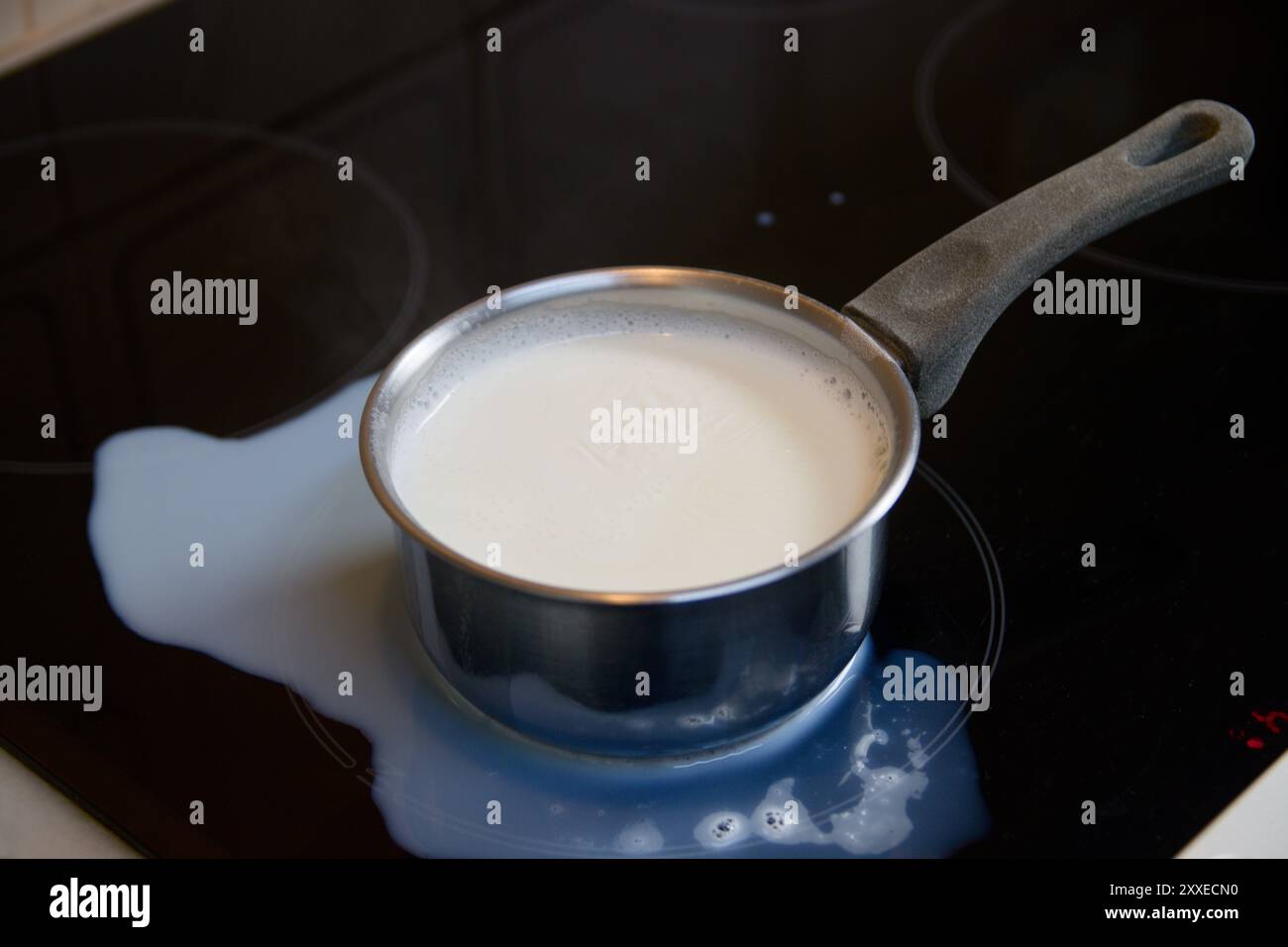 Disporre in piano una pentola con latte bollito versato su un piano cottura a induzione con vetro nero Foto Stock Disporre in piano una pentola con latte bollito versato su un piano cottura a induzione con vetro nero Foto Stock