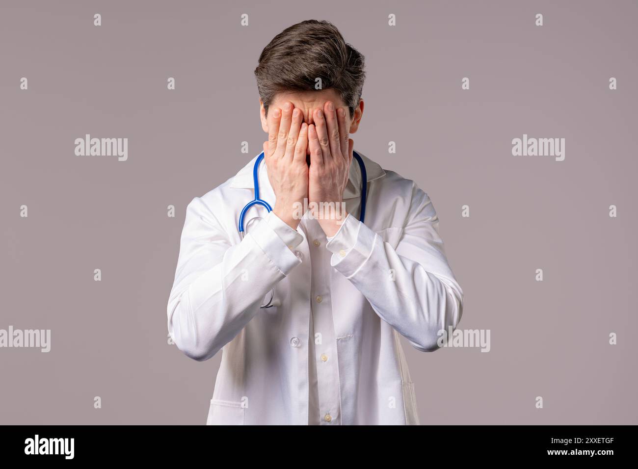 Uomo medico deluso in forma di cappotto medico bianco facendo palmo facciale. Sentimento di rimpianto, fallimento, insoddisfazione, spreco di tempo, problemi in clinica, bianco Foto Stock