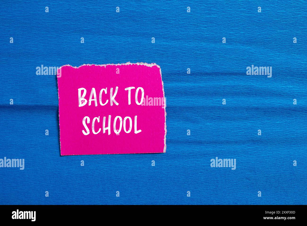 Messaggio di ritorno a scuola scritto su un pezzo di carta rosa strappato con sfondo blu. Simbolo concettuale di ritorno a scuola. Copia spazio. Foto Stock