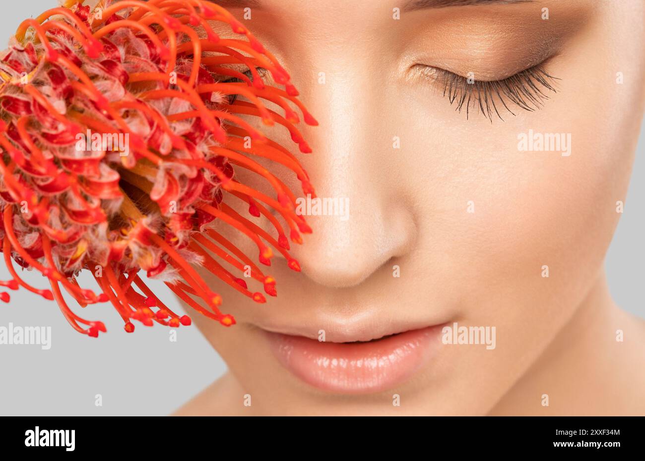 Ritratto di una ragazza affascinante con fiori, trucco, sopracciglia lussureggianti e labbra morbide. Cura della persona, cosmetologia e concetto di trucco. Foto Stock