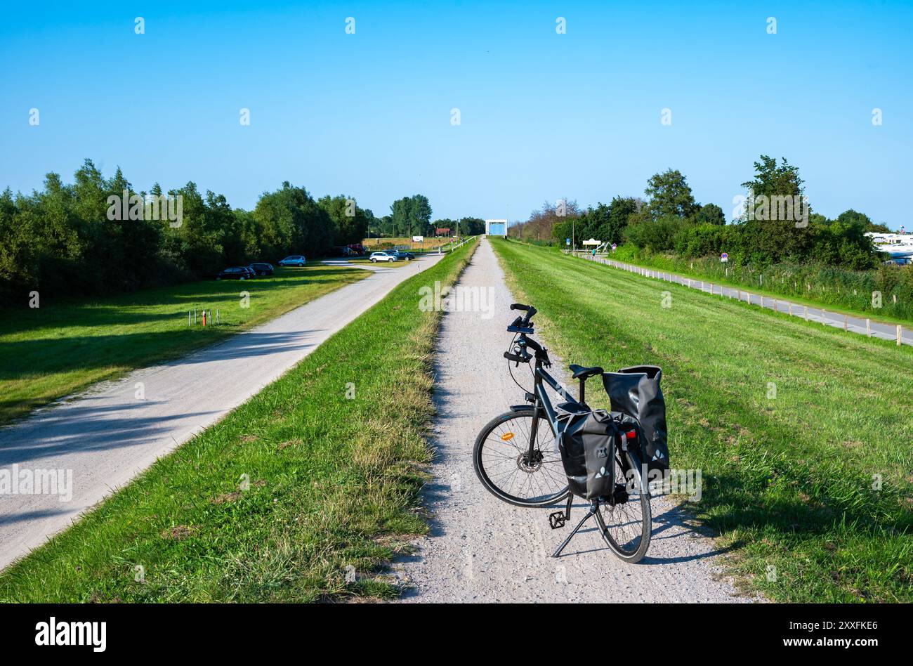 Grömitz, Germania, 20 luglio 2024 - pista ciclabile di ghiaia sulla diga verde sul mare con una bici da trekking e panieri Foto Stock