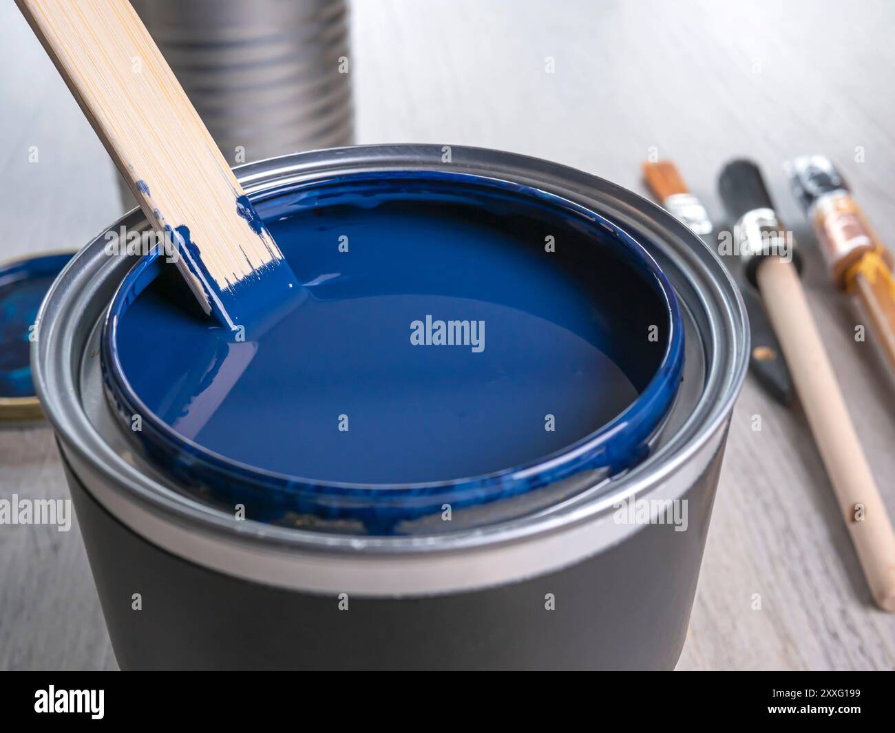 Una lattina di vernice blu con un bastoncino di miscelazione, primo piano. Pulire le spazzole di vernice sullo sfondo Foto Stock