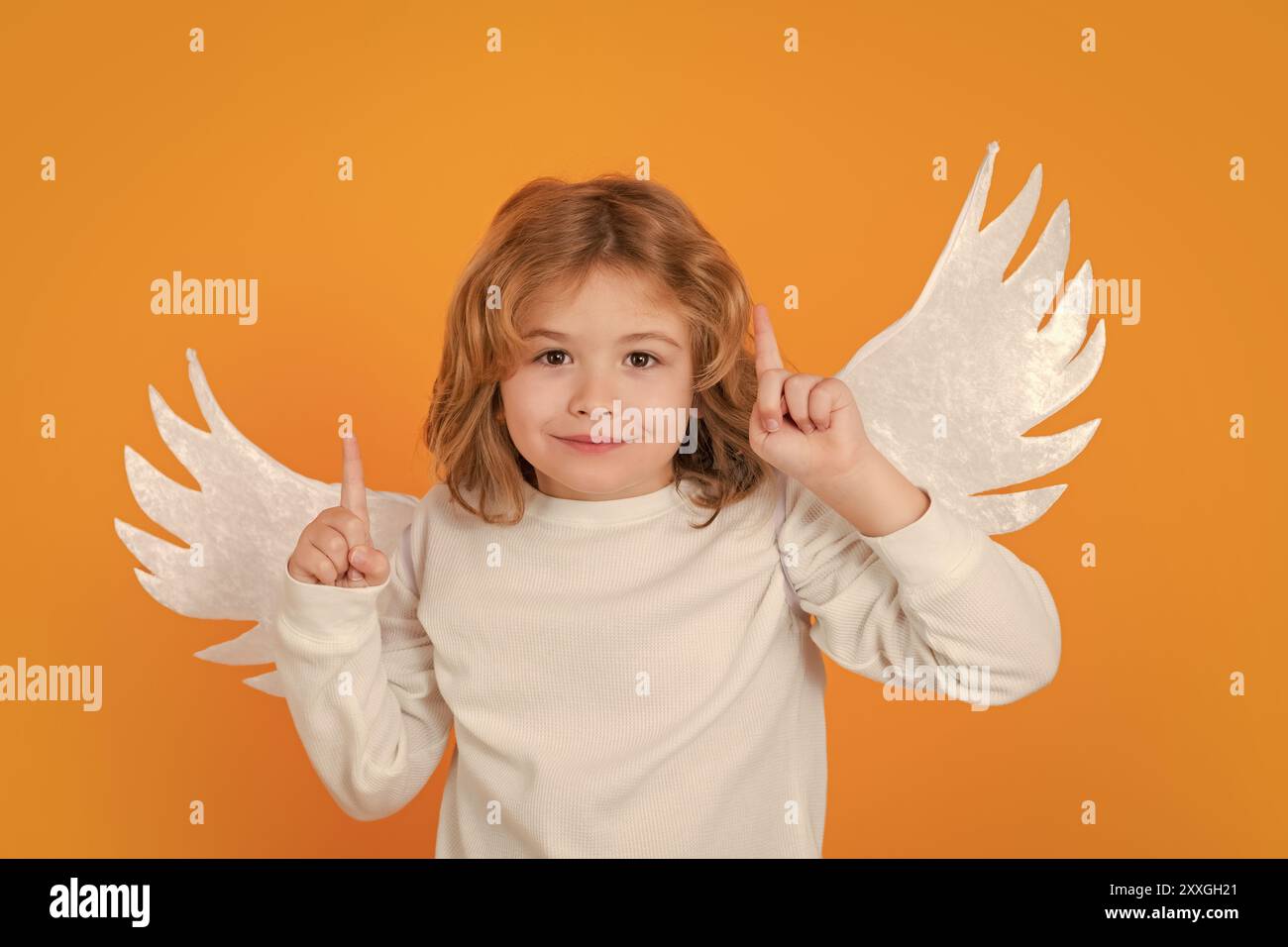 Angelo bambino che indica, gesto punto, idea. San Valentino. Bionda carino bambino con ali d'angelo su uno sfondo giallo studio. Felice angelo bambino. Foto Stock