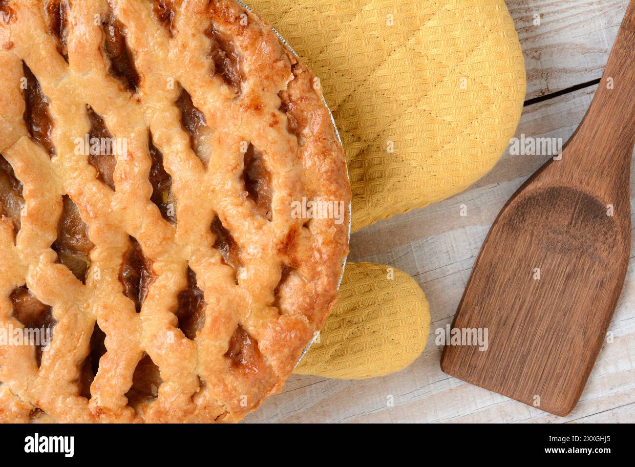 Colpo ad angolo alto di una torta di mele appena sfornata con crosta a reticolo su un guanto da forno. Formato orizzontale su un tavolo da cucina rustico in legno bianco. Foto Stock