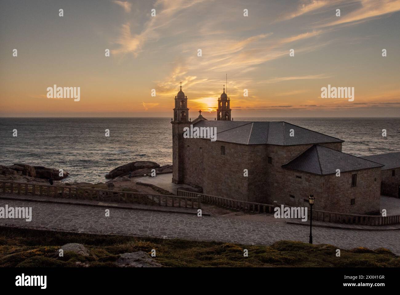 La chiesa sulle rocce al tramonto: Il Santuario della Vergine della barca, Santuario da Virxe da barca, è un punto di riferimento di Muxia, uno dei luoghi più occidentali della Spagna. Situato sulla pericolosa costa galiziana che si è guadagnata il nome di Costa da morte, è un punto di riferimento e una popolare destinazione finale per i pellegrini sul cammino di Santiago. Foto Stock