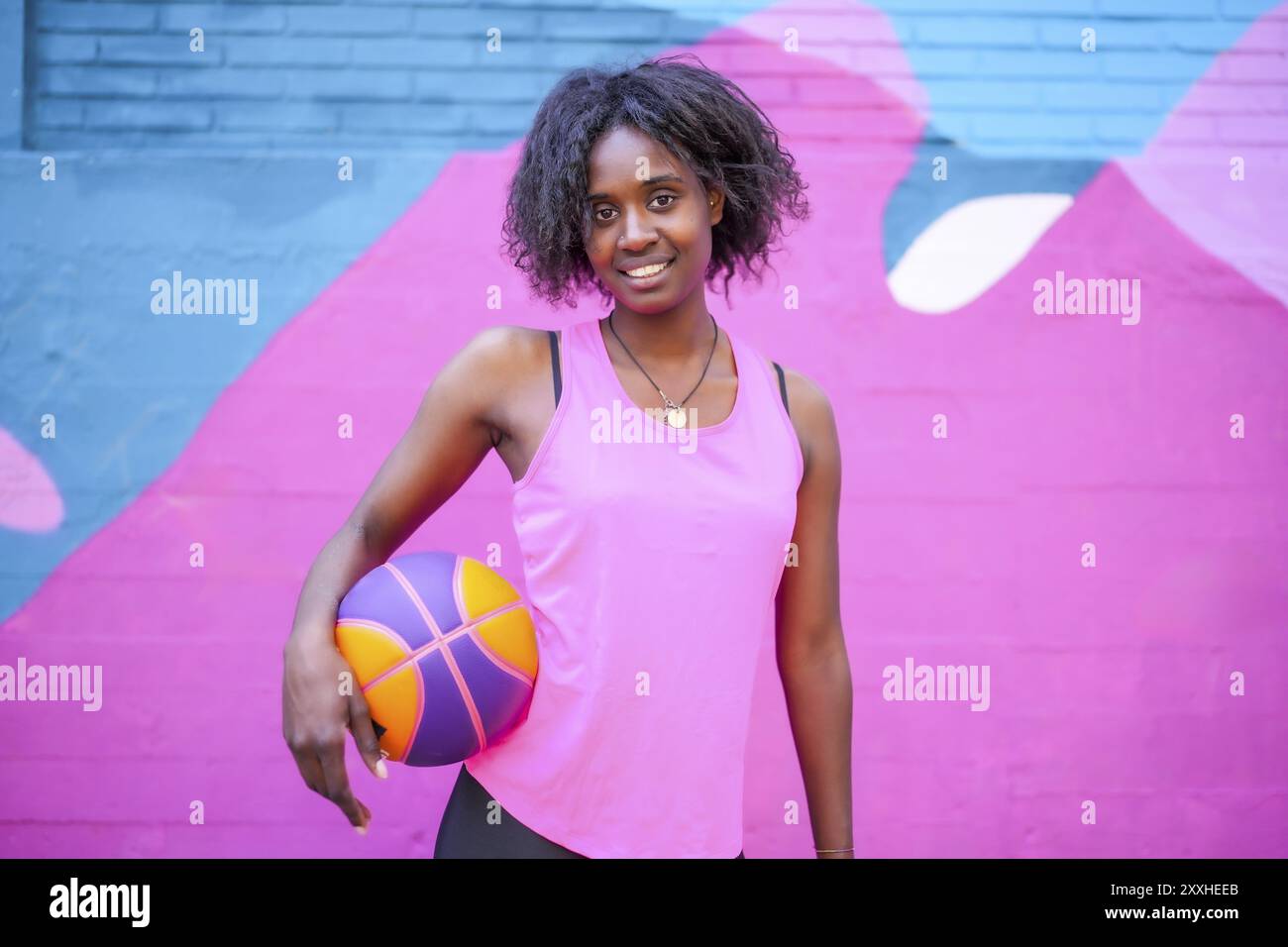 Ritratto di una felice giocatrice di basket africana contro il colorato muro urbano Foto Stock