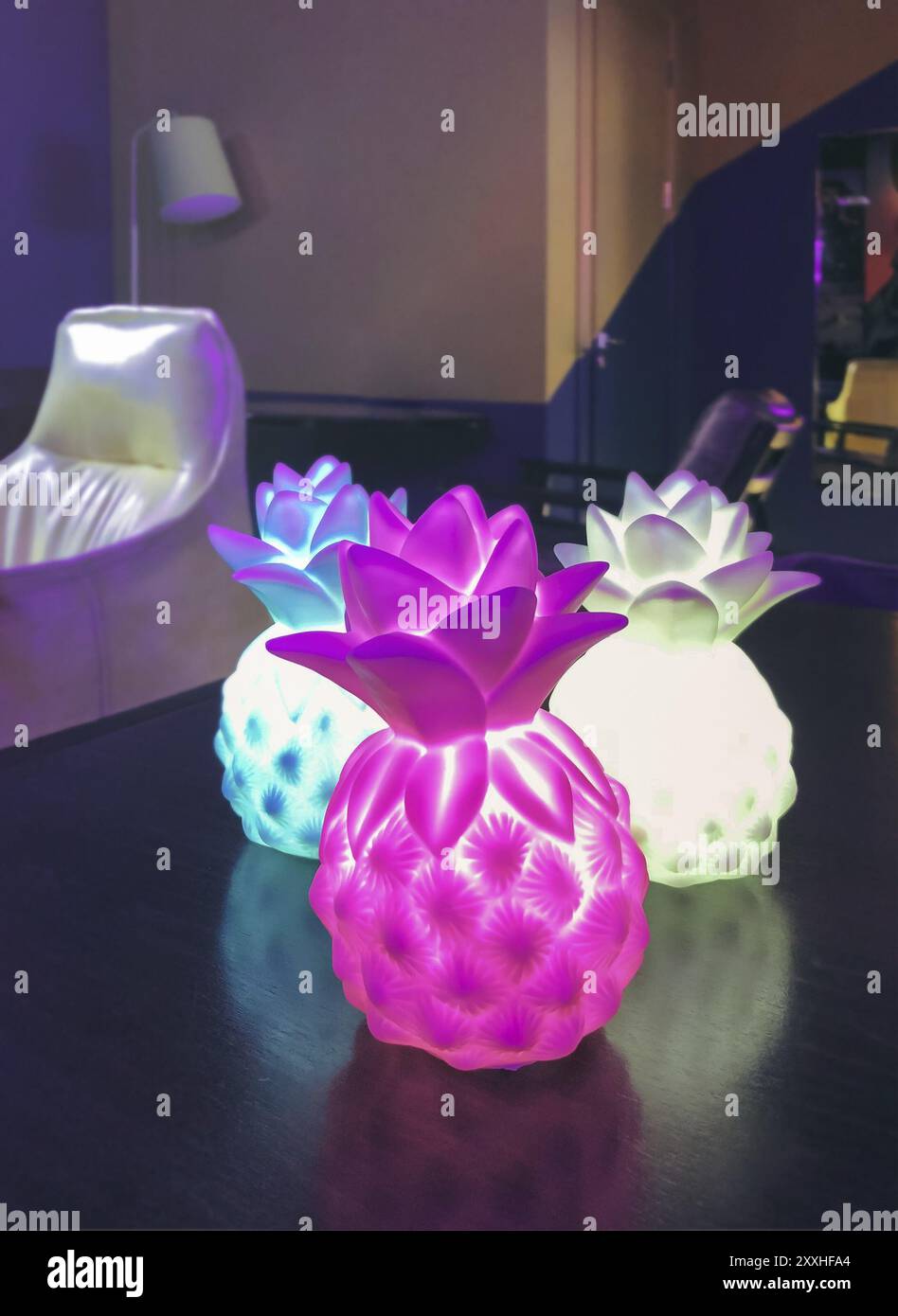 Lampade creative a forma di ananas poste su tavolo di legno illuminando scuro accogliente soggiorno in serata Foto Stock