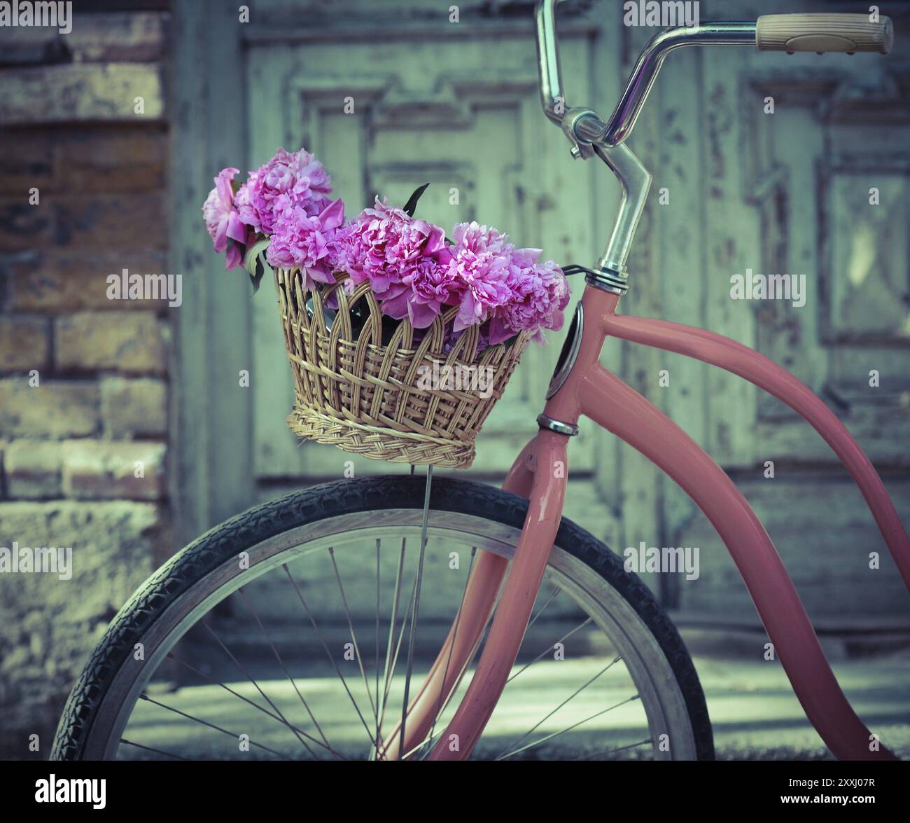 Vintage bicicletta con cestello con peonia fiori vicino alla vecchia porta di legno Foto Stock