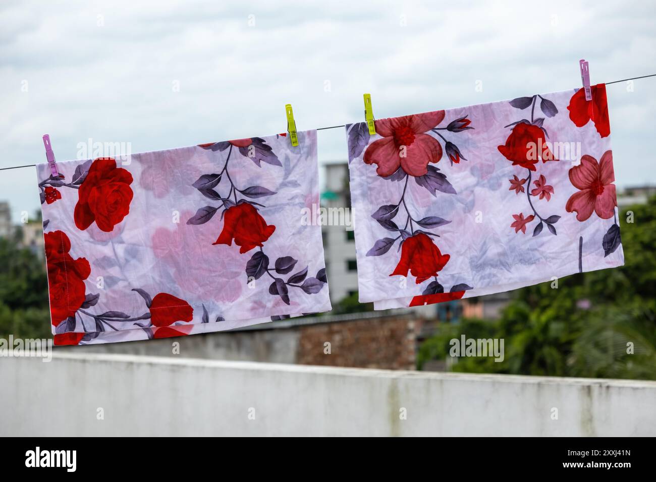 Due fodere di cuscini con stampa floreale bianca sono appese su una stoffa per asciugarsi sul tetto di un edificio in Bangladesh. Foto Stock