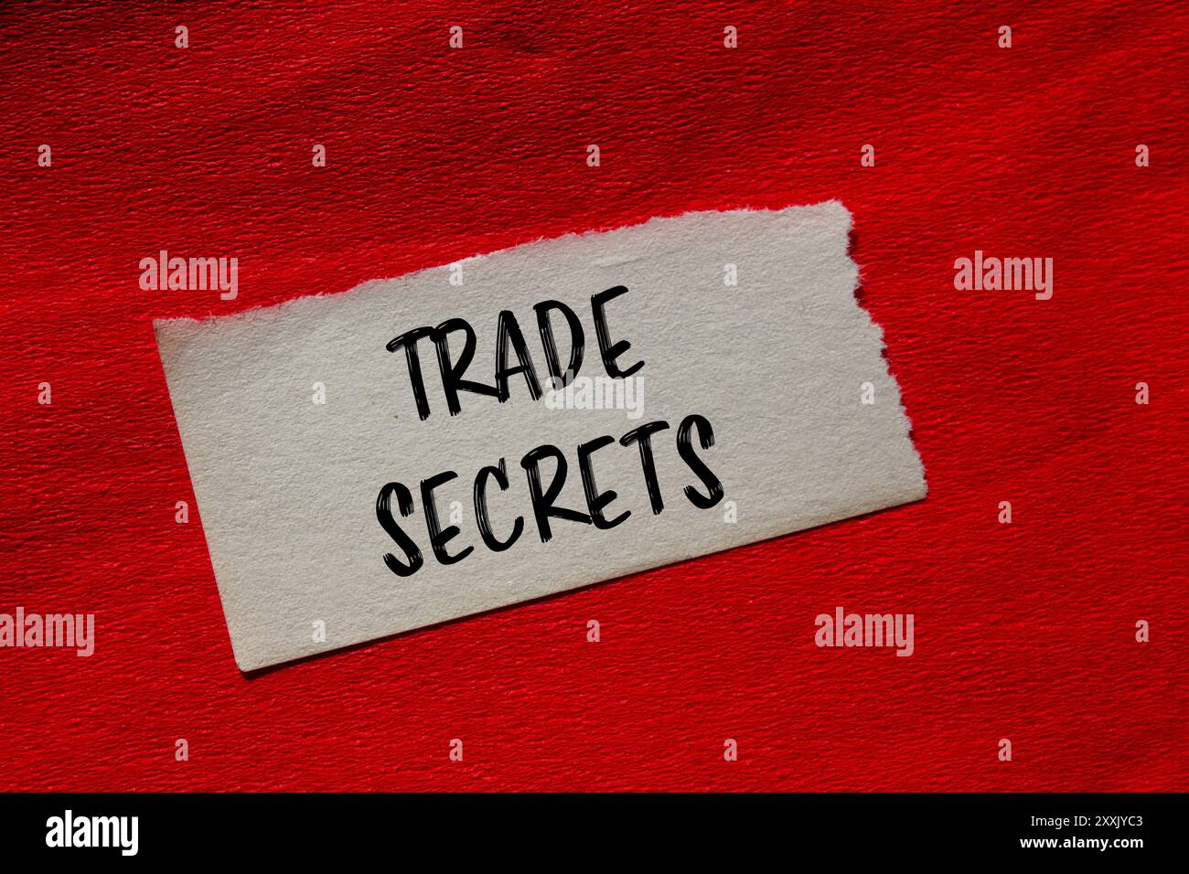 Messaggio segreto commerciale scritto su un pezzo di carta strappato con sfondo rosso. Simbolo dei segreti commerciali concettuali. Copia spazio. Foto Stock
