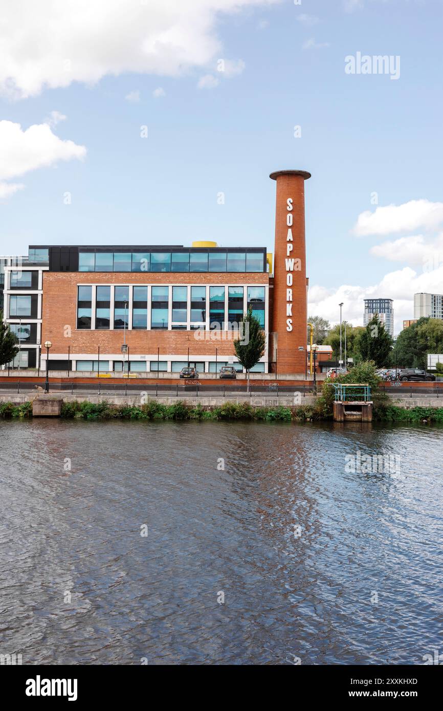 Salford, Greater Manchester, Regno Unito. 24 agosto 2024: Un moderno edificio industriale con "SOAPworks" scritto su un alto camino cilindrico si trova accanto a un c Foto Stock