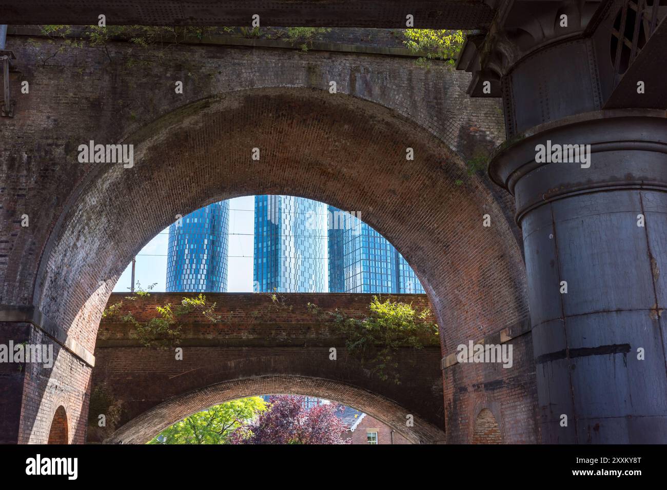 Manchester, Greater Manchester, Regno Unito. 24 agosto 2024: Una vista dei moderni grattacieli attraverso archi in mattoni storici e la vecchia infrastruttura ferroviaria. Foto Stock