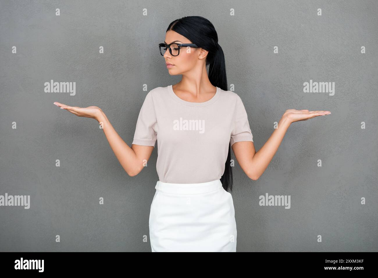 Cosa scegliere? Giovane donna d'affari sicura di sé che tiene gli spazi di copia sulle mani mentre si trova su sfondo grigio Foto Stock