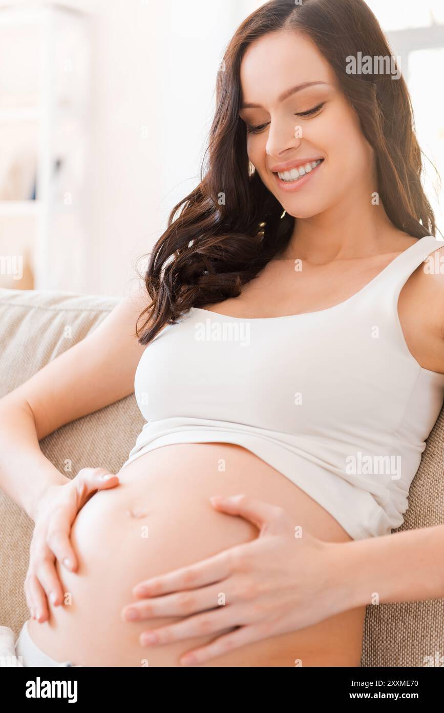 Non vedo l'ora di incontrarti. Ritratto di una giovane donna incinta che le tocca la pancia e sorride Foto Stock
