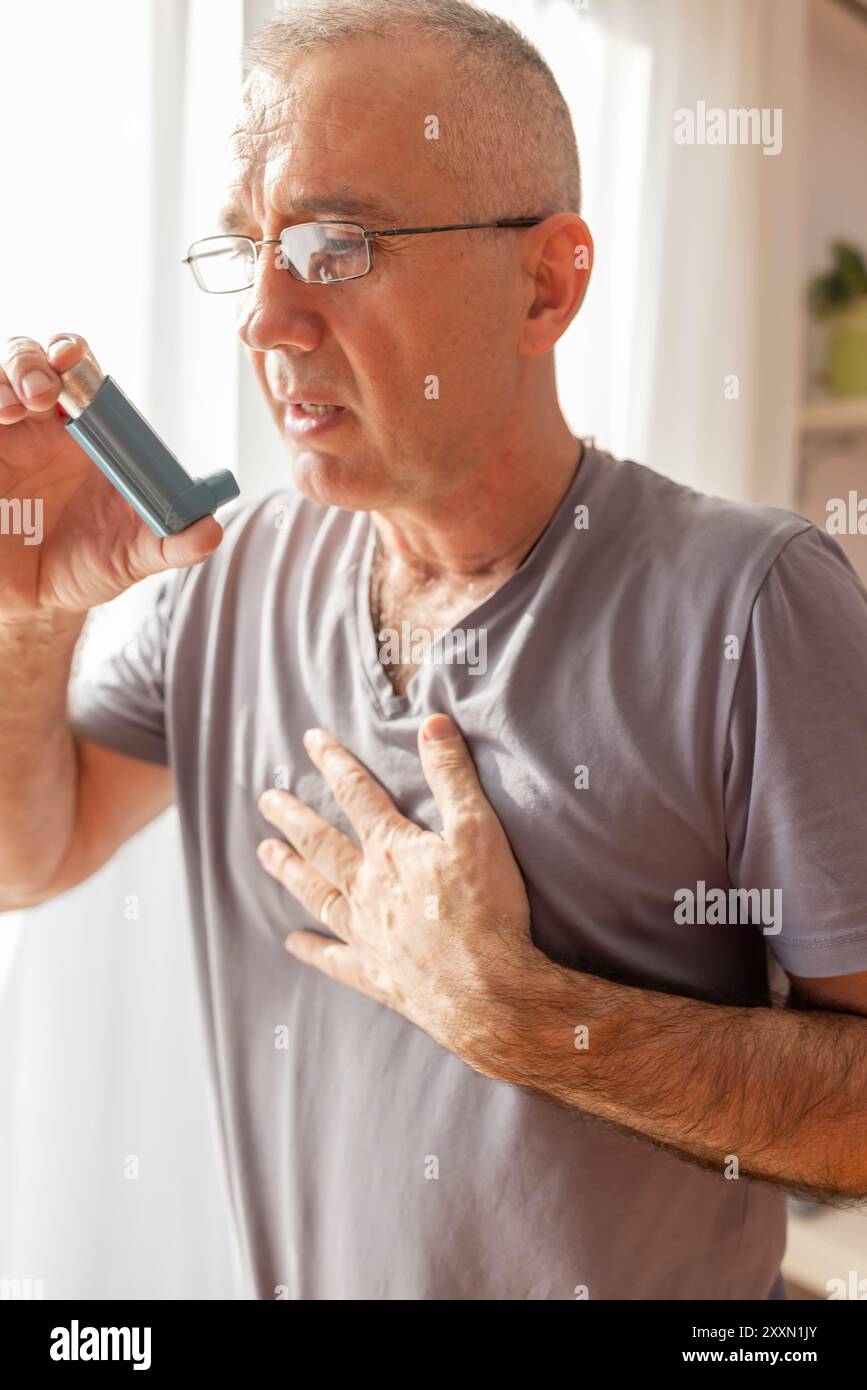 Un uomo asmatico maturo che prende un inalatore e ha un attacco d'asma. Ha un problema con l'asma e ha un inalatore. Foto Stock