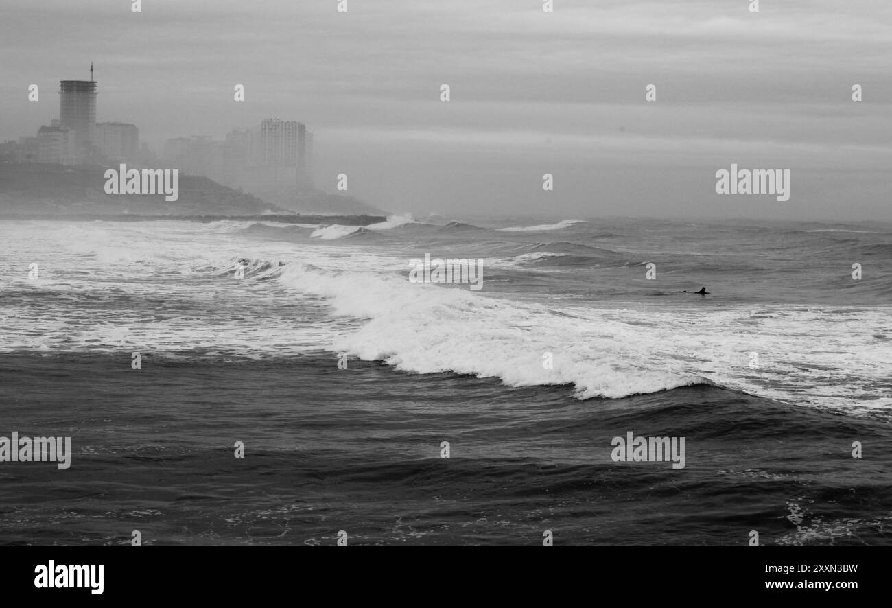 foto in bianco e nero dell'oceano con paesaggio urbano sullo sfondo in bianco e nero Foto Stock