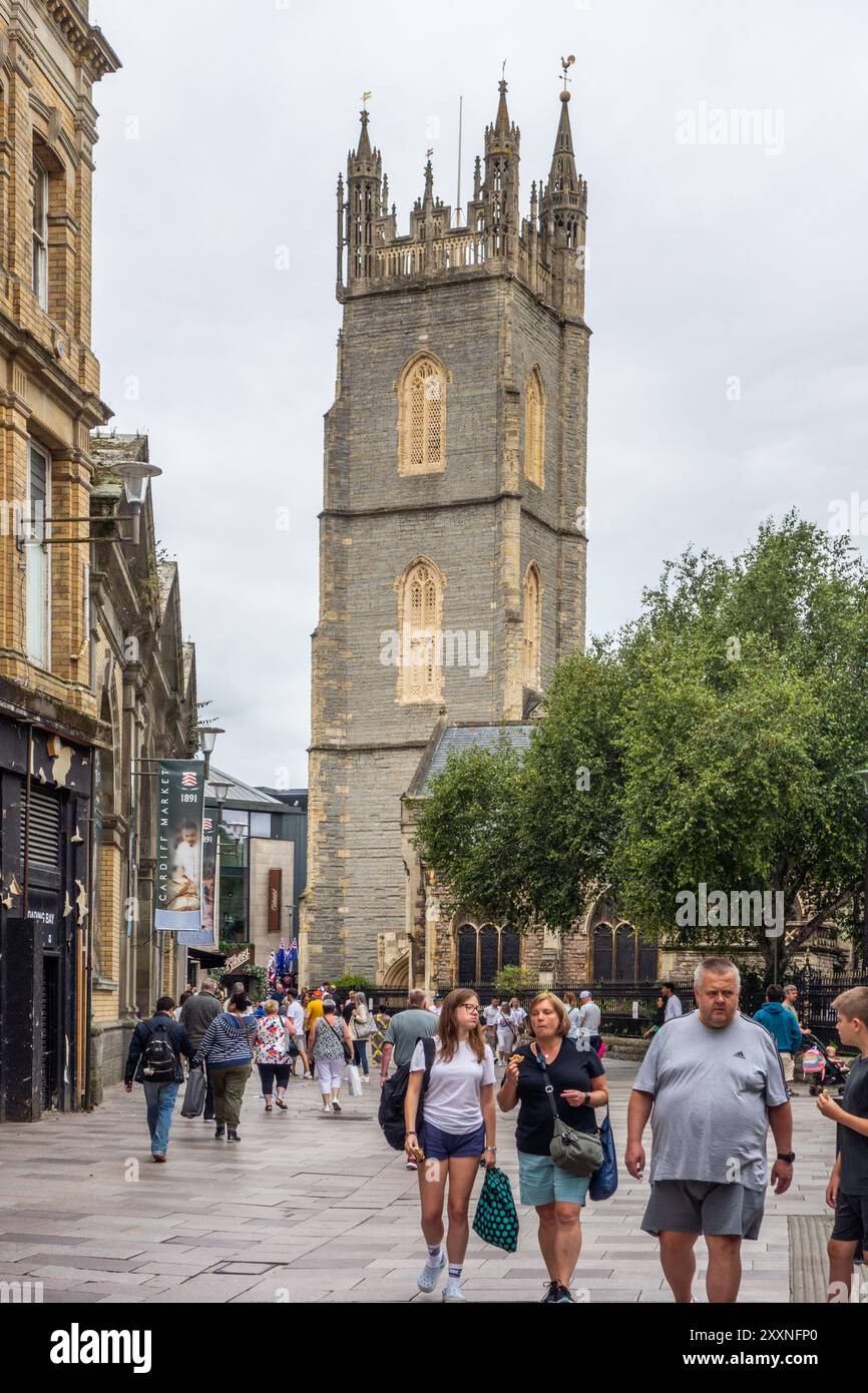 Persone che fanno shopping e turisti lungo Trinity Street, nella capitale gallese di Cardiff, con vista sulla chiesa parrocchiale di San Giovanni Battista. Foto Stock
