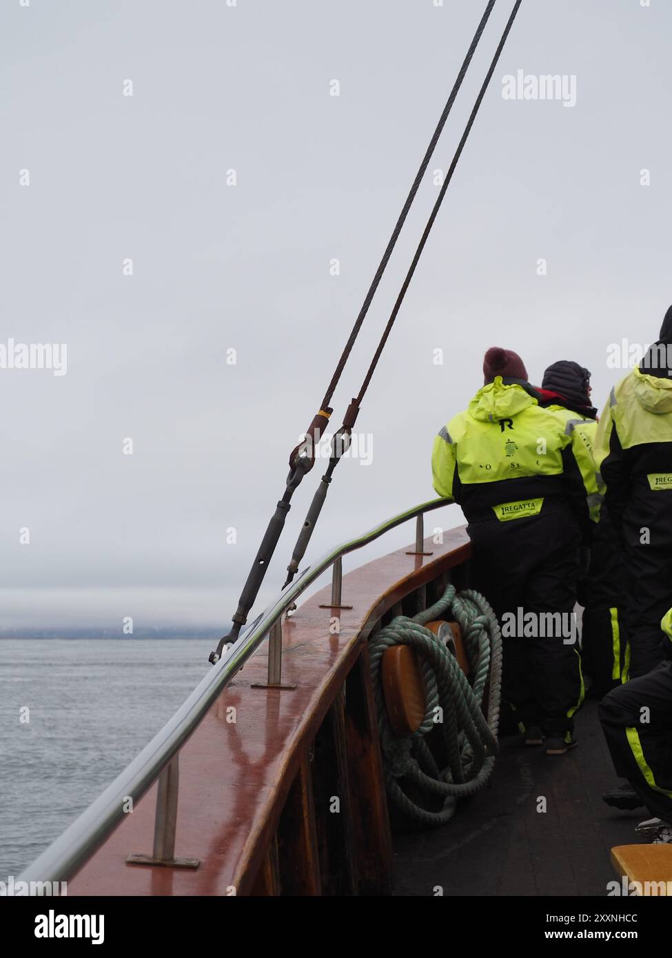 Husavik, Islanda - 12 maggio 2024: Le persone in tute di sopravvivenza brillanti stanno su una barca mentre naviga attraverso un mare freddo e grigio, simboleggiando la resilienza umana e. Foto Stock