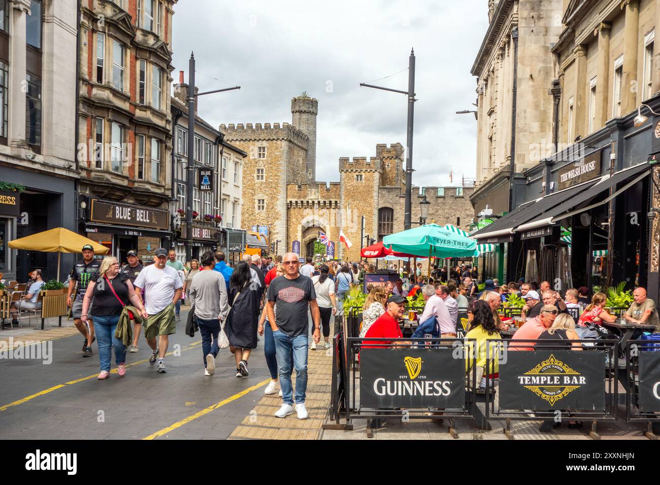 Persone che amano il clima caldo, mangiano e bevono all'aperto lungo High Street, nella capitale gallese di Cardiff, con vista sul castello di Cardiff Foto Stock