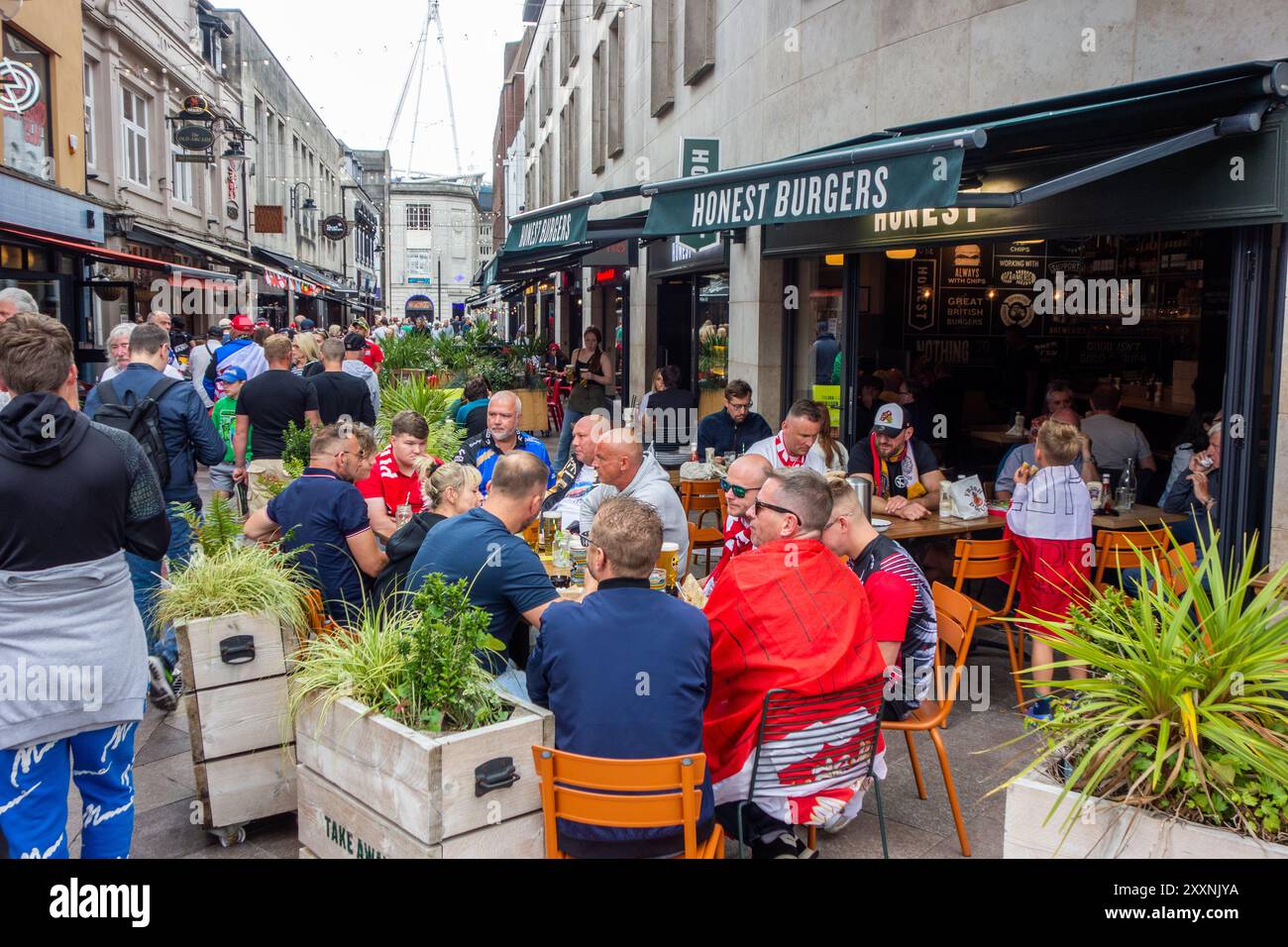 Persone che amano il clima caldo, mangiano e bevono all'aperto lungo High Street, nella capitale gallese di Cardiff, con vista sul castello di Cardiff Foto Stock