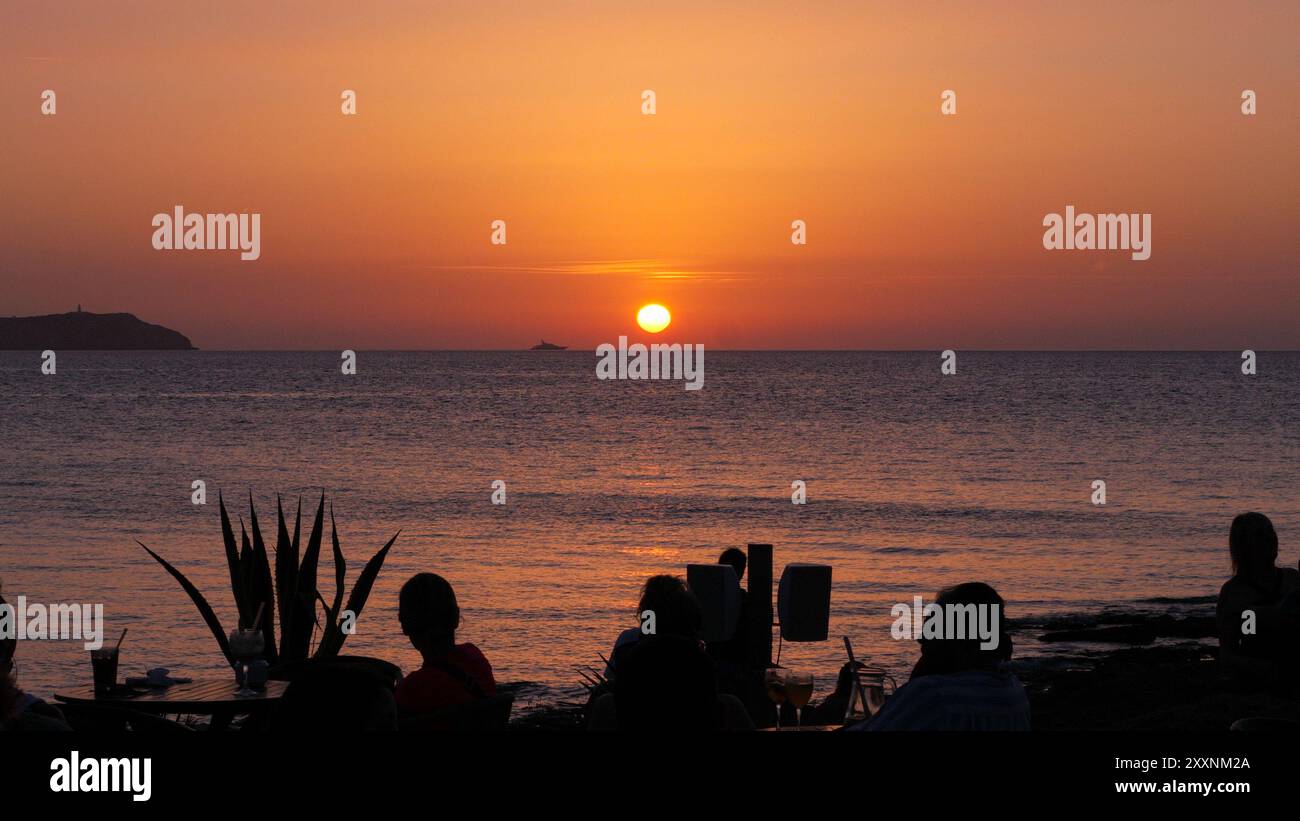 Tramonto sul Mar Mediterraneo a San Antonio, Ibiza, Spagna, con la silhouette di persone sedute in un bar all'aperto che sorseggia un drink al tramonto. Foto Stock
