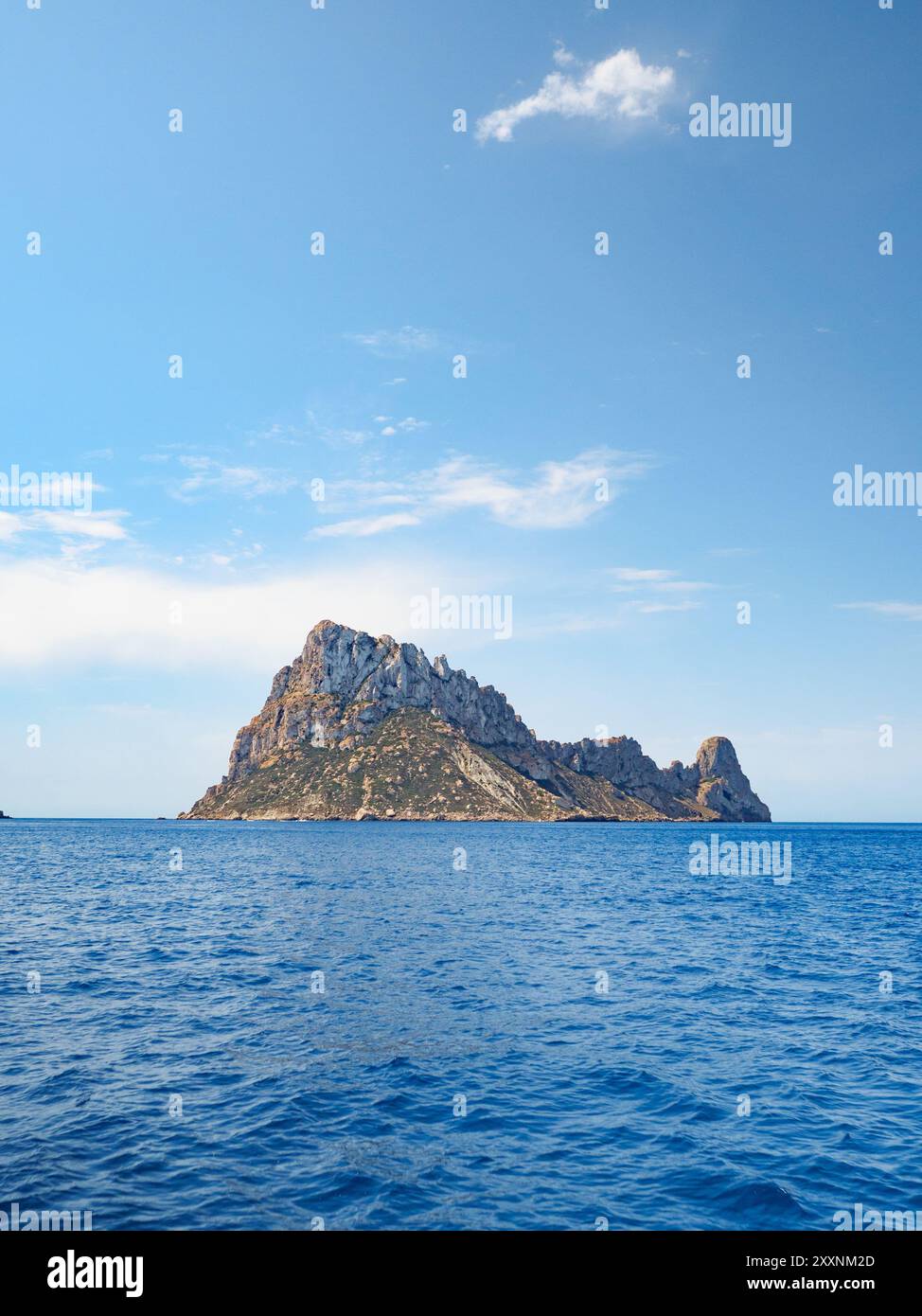 Foto diurna dell'isola di es Vedra, al largo della costa di Ibiza, scattata dal mare, con cieli blu e alcune nuvole visibili all'orizzonte Foto Stock