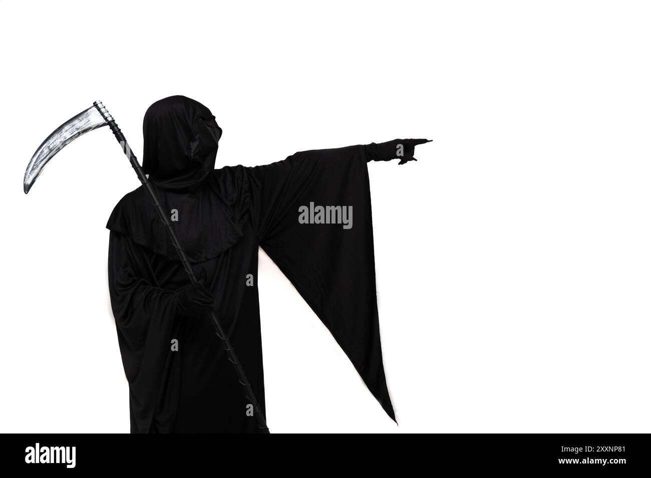 Il triste mietitore, vestito con un costume di Halloween con un mantello scuro, tiene una falce in una mano e punta minacciosamente verso lo spazio vuoto con l'ot Foto Stock