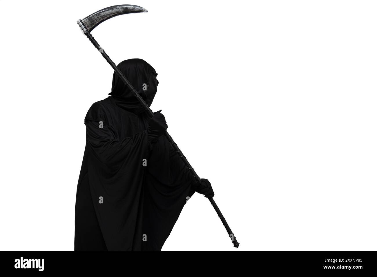 Il triste mietitore, vestito con un costume di Halloween con un mantello scuro, tiene una falce minacciosamente, puntandola verso lo sfondo bianco vuoto del copyspace Foto Stock