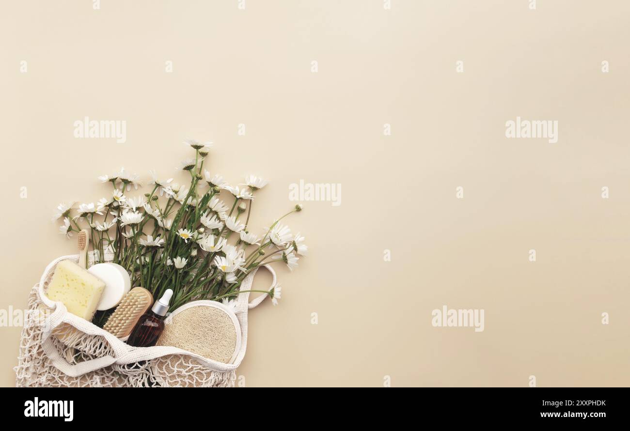 Eco friendly concetto estivo su sfondo beige con borsa eco shopping, fiori camomilla bianchi, accessori bagno, spazzole, bottiglia di olio essenziale, sapone Foto Stock