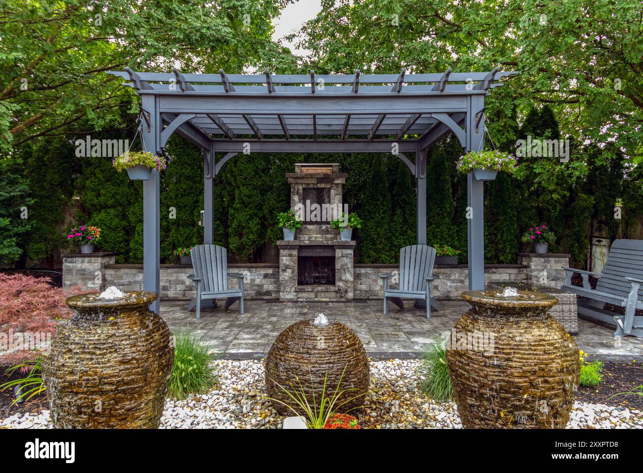 Grande pergola grigia su asfaltatori con caminetto in pietra e urne a cascata per un paesaggio da oasi nel cortile Foto Stock