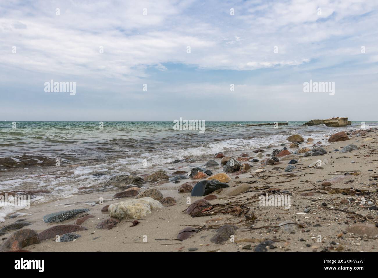 Costa baltica rocciosa con ciottoli, sabbia, onde e un cielo blu nuvoloso Foto Stock