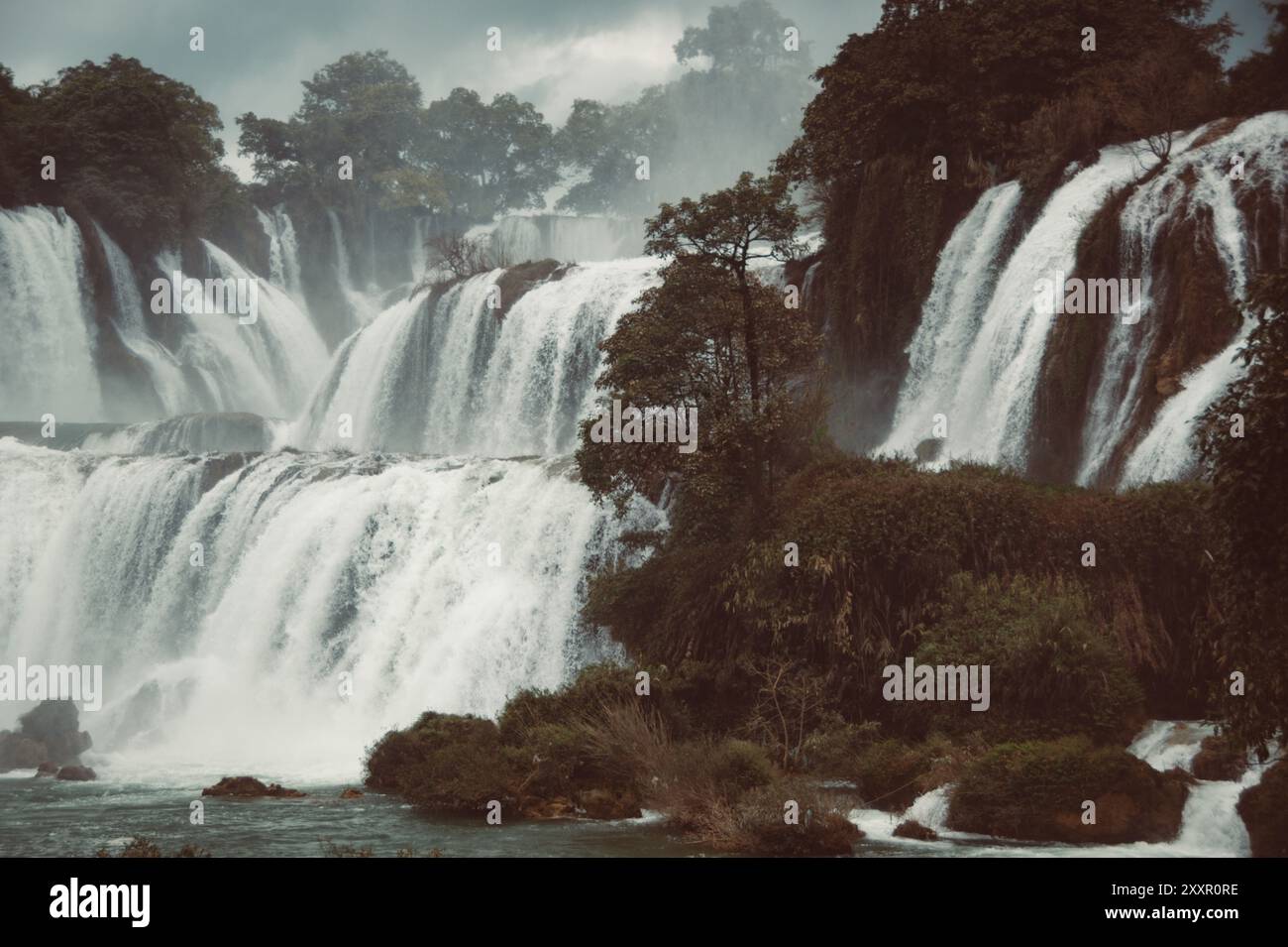 Le potenti cascate scorrono su aspre scogliere, circondate da vegetazione lussureggiante e nebbia sotto un cielo spettacolare e nuvoloso. Foto Stock