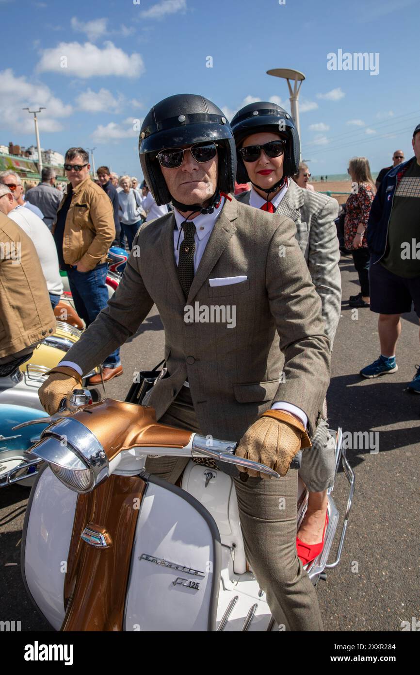 Una coppia che indossa abiti in tweed guida uno scooter. Migliaia di persone partecipano all'annuale Mod Weekender che si tiene nella cittadina costiera inglese di Brighton. Quest'anno celebra il 60° anniversario della battaglia di Brighton, una delle più famose battaglie di Brighton tra i Mods e i Rockers. Negli anni '1950 e '1960 le due sottoculture giovanili si sono riunite nelle località balneari dell'Inghilterra meridionale per combattere le battaglie tra loro e la polizia. Ciò causò una protesta morale pubblica da parte di una società conservatrice del dopoguerra che vide gli autori arrestati, processati e imprigionati. Mentre la cultura Rocker è le Foto Stock