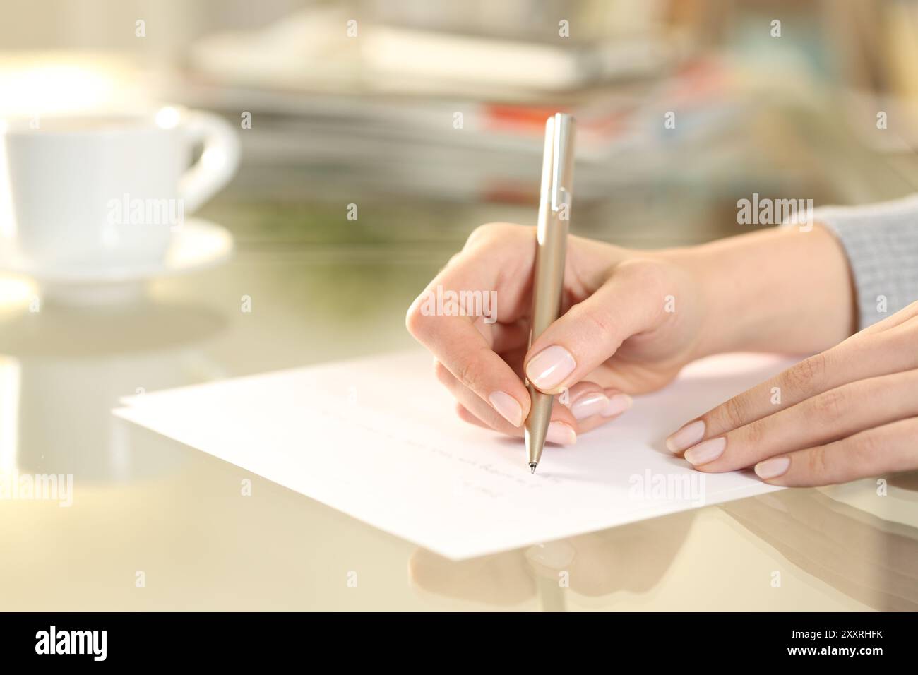 Primo piano di una donna che scrive a mano su un foglio di carta su una scrivania a casa Foto Stock