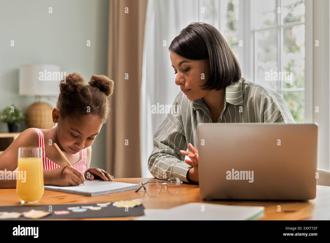 Madre afroamericana che lavora al portatile a casa con la figlia Foto Stock