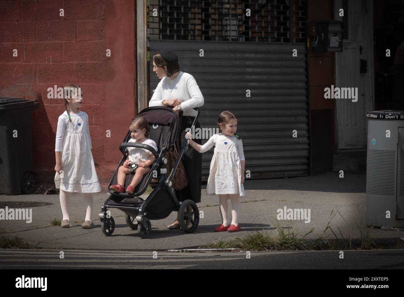 Una madre ebrea ortodossa di 3 pause per parlare con le sue ragazze, 2 delle quali indossano gli stessi vestiti. A Brooklyn, New York, 2024. Foto Stock