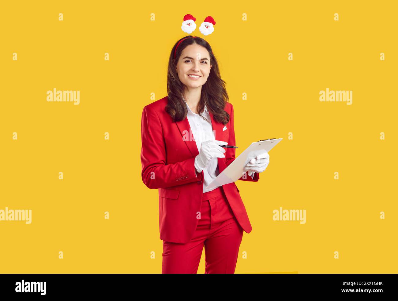 Donna sorridente che indossa in stile Babbo Natale con corna di Natale che prendono appunti in blocchi per appunti su sfondo giallo. Foto Stock