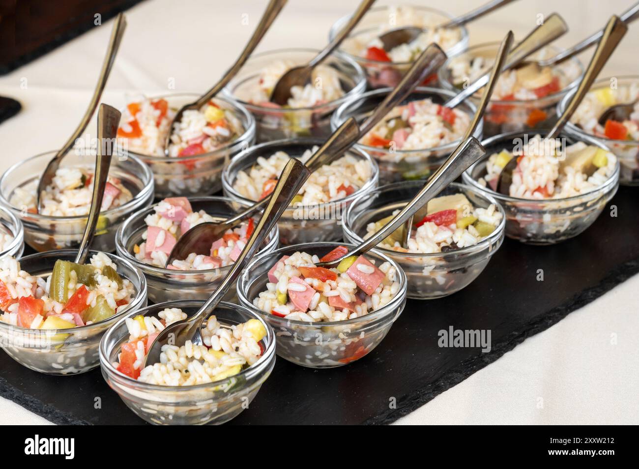 Dall'alto delle ciotole di vetro assortite ripiene di insalata di riso con preparazione di verdure e cucchiai mentre sono disposte ordinatamente sul tavolo da pranzo sotto le luci Foto Stock