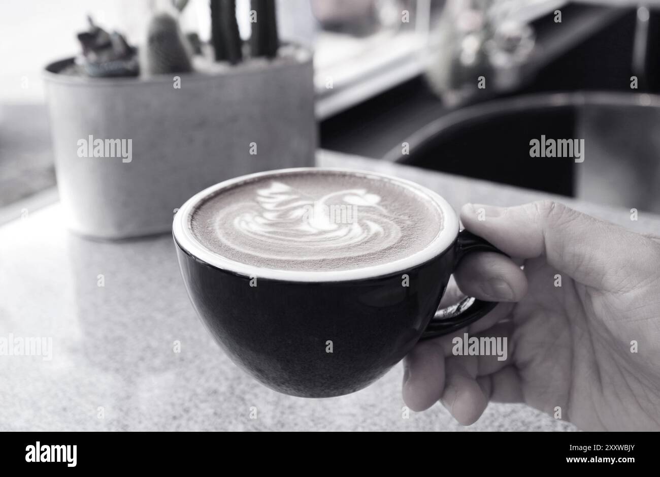 Immagine monocromatica di una mano che regge una tazza di caffè cappuccino con una latte art unica Foto Stock