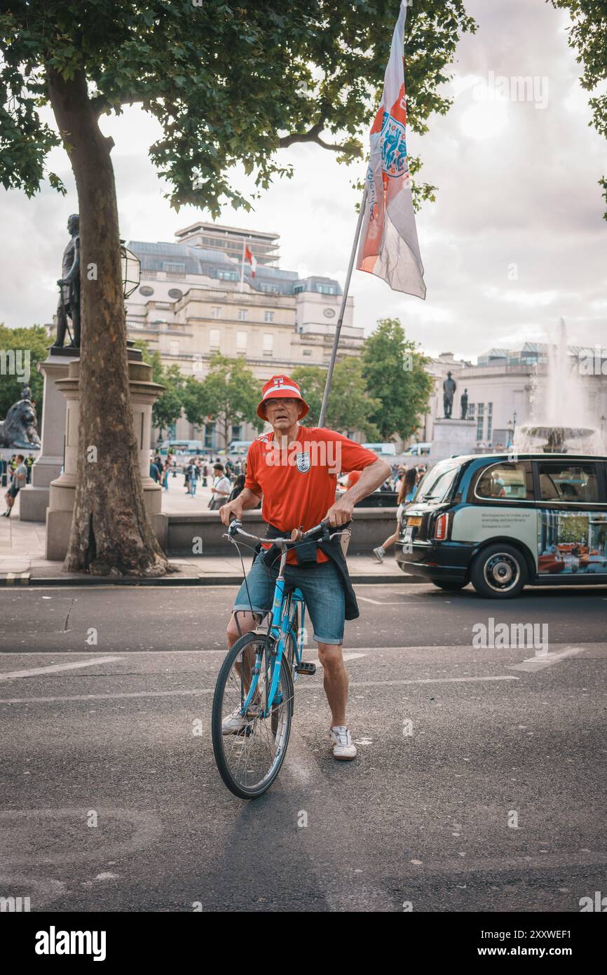 Euro Finals - Londra - Regno Unito - 2024.07.14: Un appassionato di calcio che indossa una maglietta e un berretto inglese corre in bicicletta con una bandiera nel centro di Londra durin Foto Stock